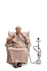 Mature man in ethnic clothes sitting in an armchair and smoking shisha