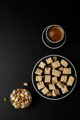 Halva with pistachios served with coffee on black. Traditional middle eastern sweets. Jewish, turkish, arabic national dessert. Turkish delight concept. Natural vegan product. Top view. Copy space.
