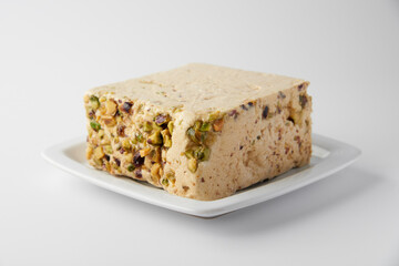 Organic halva with pistachios on a white plate isolated on white. Traditional middle eastern sweets. Jewish, turkish, arabic oriental national dessert. Turkish delight concept. Natural vegan product.