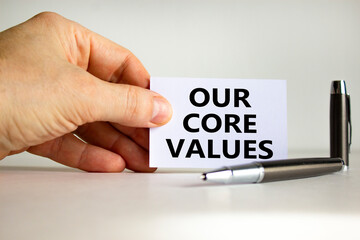 Our core values symbol. White paper with words 'Our core values' in businessman hand, metallic pen. Beautiful white background. Business, our core values concept. Copy space.
