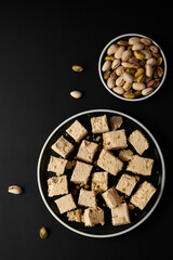 Organic halva with pistachios on black background. Traditional middle eastern sweets. Jewish, turkish, arabic national dessert. Turkish delight concept. Natural vegan product. Top view. Copy space.