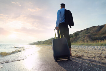 Businessman with suitcase walking on beach, low angle view. Business trip