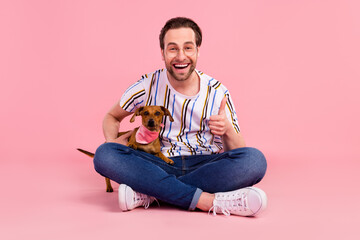 Full length photo of cheerful happy young man make thumb up hold dog smile isolated on pink color...