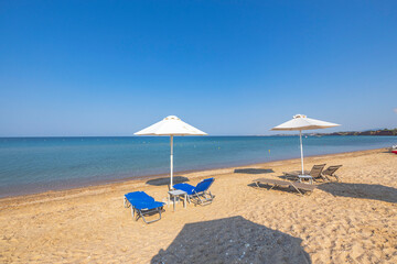 Landscape view of empty sunbeds under umbrellas on sand beach. Greece. 