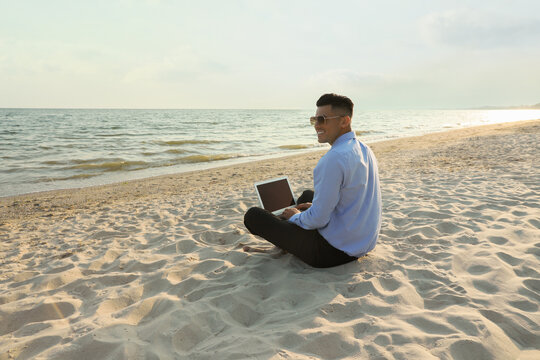 Happy businessman working with laptop on beach. Business trip