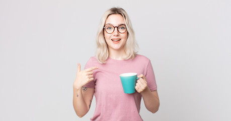 young pretty albino woman feeling happy and pointing to self with an excited with a coffee mug