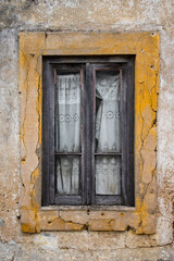 Detail of old window in abandoned rural house with wooden frame and torn lace curtains on a grungy wall with yellow paint border