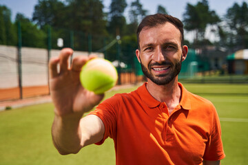 Dark-haired sportsman showing his tennis equipment for the camera - Powered by Adobe