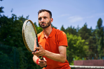 Serious focused young man playing tennis outdoors