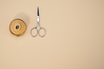 Closeup of scissors and tape measure on an aesthetic cream background.