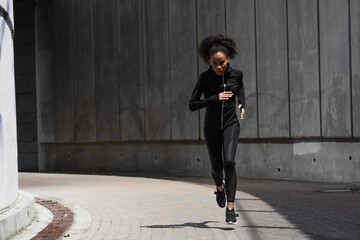 Young african american woman looking at camera while jogging on urban street