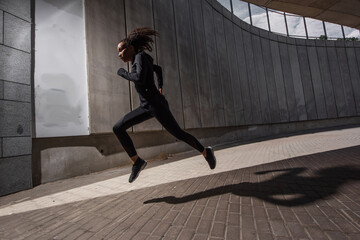 Side view of african american woman running near building with concrete facade on urban street
