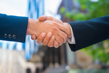 Handshake close-up. Businessman and his colleague are shaking hands in front of modern office building. Financial investors outdoor. Banking and business.