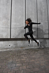Obraz na płótnie Canvas African american sportswoman in black sportswear running near concrete wall
