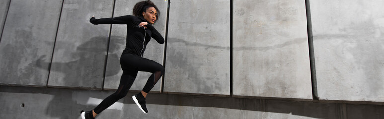African american sportswoman running near building outdoors, banner