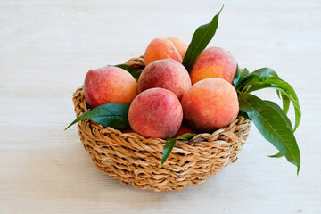 Bunch of ripe organic peaches in a wicker bowl, white wooden table background. Local produce fruits in a basket. Clean eating concept. Top view, close up, copy space for text.