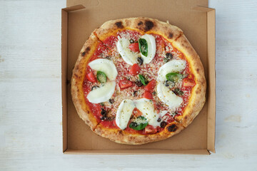 Oven baked pizza with buffalo mozzarella, parmigiano-reggiano cheese, basil and anchovies in a box....