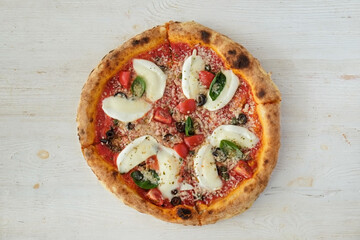Oven baked pizza with buffalo mozzarella, parmigiano-reggiano cheese, basil and anchovies. Traditional italian dish on white wood textured table background. Close up, copy space, top view.