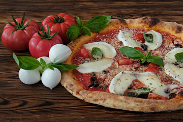 Fototapeta na wymiar Cropped shot of oven baked pizza with buffalo mozzarella, parmigiano-reggiano cheese, basil and anchovies. Traditional italian dish on wood textured table background. Close up, copy space, top view.