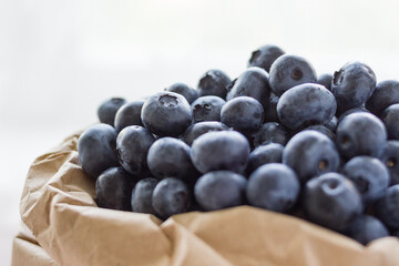 A lot of beautiful juicy fresh summer blueberries in a brown bag on a light background