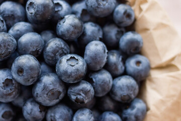 A lot of beautiful juicy fresh summer blueberries in a brown bag on a light background