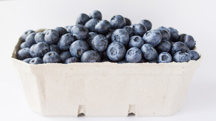 A lot of beautiful juicy fresh summer blueberries in a brown bag on a light background