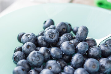 A lot of beautiful juicy fresh summer blueberries on a light turquoise glass plate
