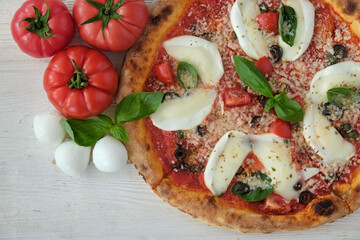 Cropped shot of oven baked pizza with buffalo mozzarella, parmigiano-reggiano cheese, basil and anchovies. Traditional italian dish on wood textured table background. Close up, copy space, top view.