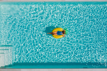 Sexy young female in swimsuit bikini, in a straw hat and sunglasses floating on blue swimming pool...