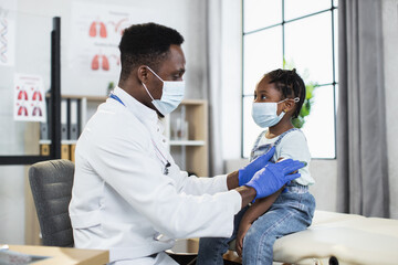 Competent male pediatrician in medical mask and gloves making Covid-19 vaccination in shoulder of...