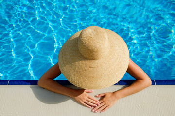 Unrecognizable caucasian woman wearing broad brim straw hat that covering her whole body, chilling in a swimming pool. Copy space, top view.