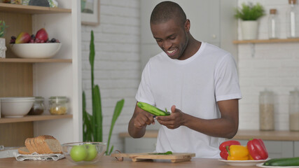 Healthy African Man Peeling Cucumber in Kitchen 