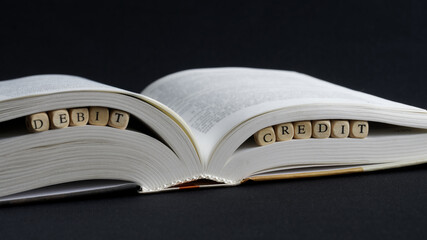 Inscription debit credit next to an open book on a dark surface. The concept of accounting and bookkeeping. Benefit decision