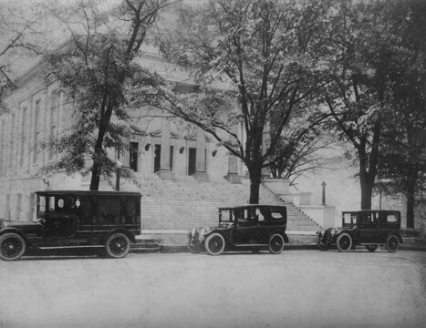 Black and white photo of old black cars parked in front of large stone courthouse building