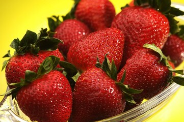 Closeup of red juicy strawberries in bowl with yellow background