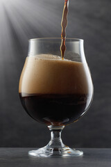 Dark beer with flowing foam head. Stream of dark stout pours into a beer glass. Selective focus