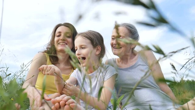 Cute child girl with her young mother and senior grandmother are having picnic during summer outdoor in nature, mothers day, happy retirement, multi generation family
