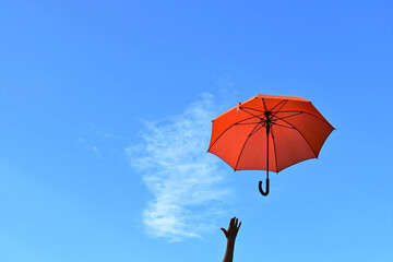 orange umbrella flying away into the blue sky and a child's hand. Weather changes, strong wind. Background. Copy space