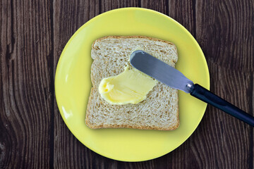 Buttering the bread. Loaf of bread on a yellow plate on a wooden table.