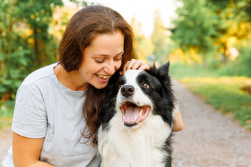 Smiling young attractive woman playing with cute puppy dog border collie on summer outdoor background. Girl holding embracing hugging dog friend. Pet care and animals concept