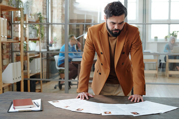 Serious hr manager bending over table while looking through resume of applicants
