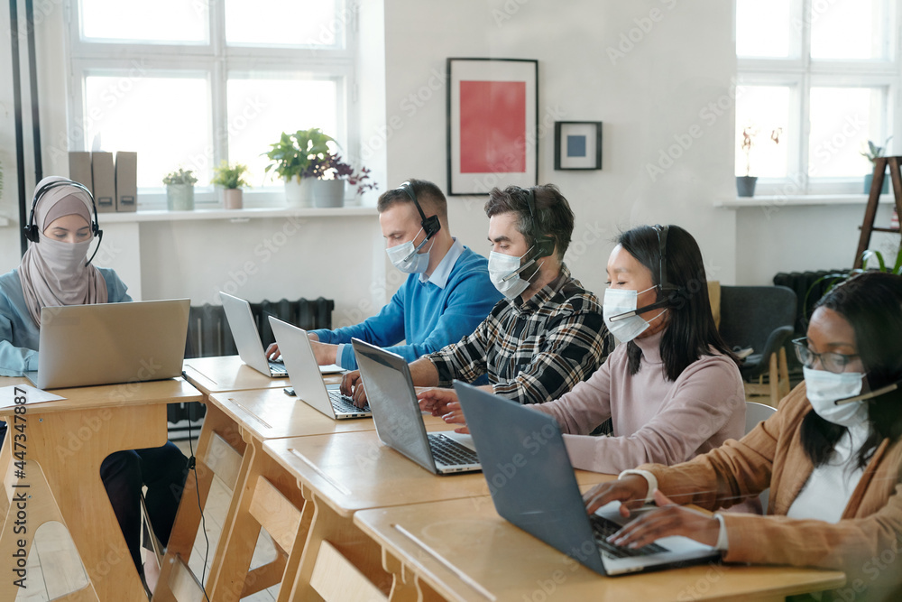 Poster Large group of operators in masks consulting online clients in front of laptops