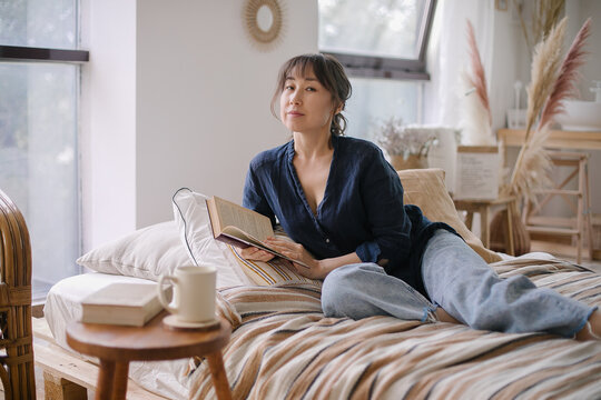 Beautiful young Asian woman reading a book. Enjoying a quiet time and relaxing environment at cozy home