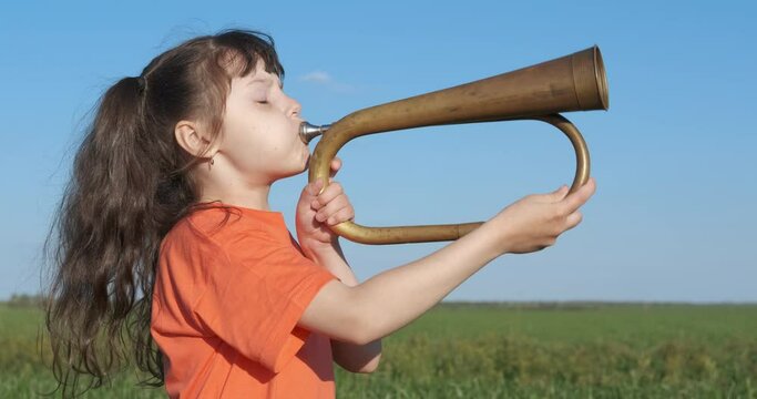 Kid with a pipe in the fresh air. Cute little girl blows in the bugle in nature.