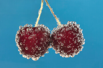 Two isolated red cherries in sparkling water with blue background