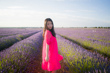 young Asian woman outdoors at lavender flowers field - happy and beautiful Korean girl in sweet Summer magenta dress enjoying holidays relaxed on purple floral meadow