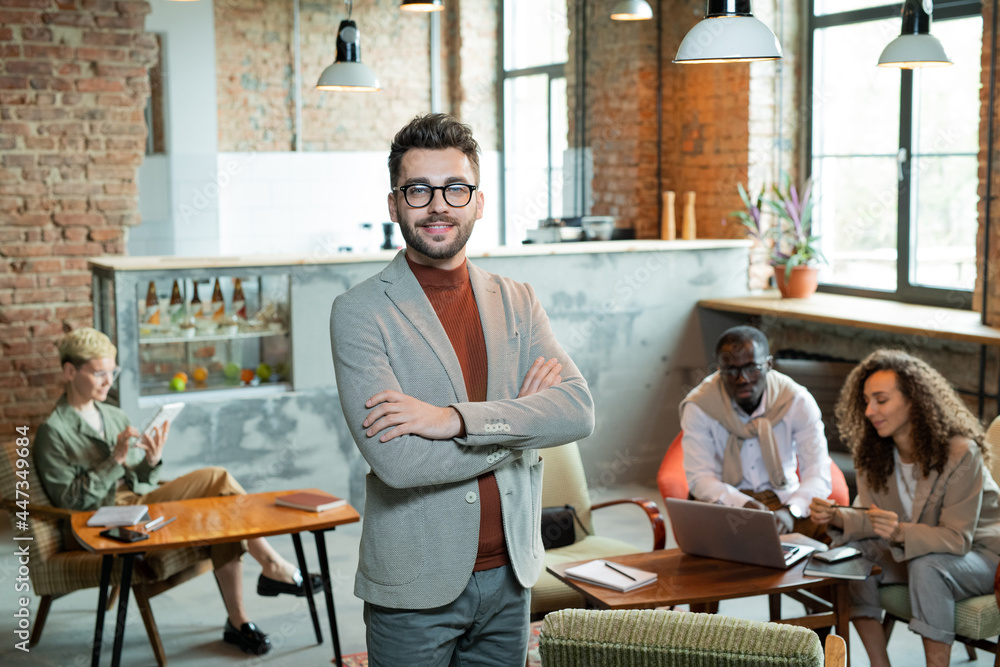 Poster young smiling cross-armed businessman standing in front of working colleagues