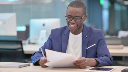 Fototapeta premium Young African Businessman Celebrating Success While Reading Documents