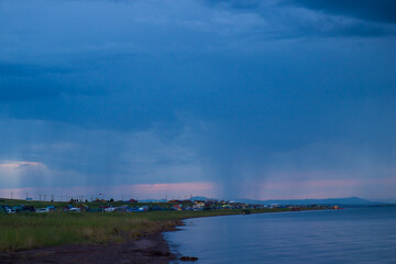 Tent camp on the shore of the lake. Camping summer vacation by the water. Landscape at sunset during the rain