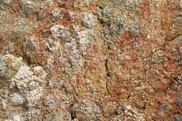 The textured surface of dried red, brown and gray clay is covered with cracks. The surface is similar to Martian soil. Top view, textured, background.